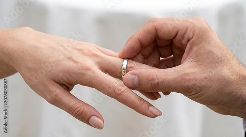 A close-up of a person placing a wedding ring on another person's finger during a wedding ceremony, symbolizing commitment and love