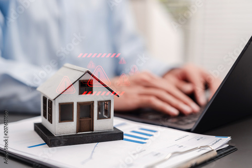 Mortgage risk and high interest rate danger concept. Miniature house with red warning alert icons and man using laptop on financial charts.