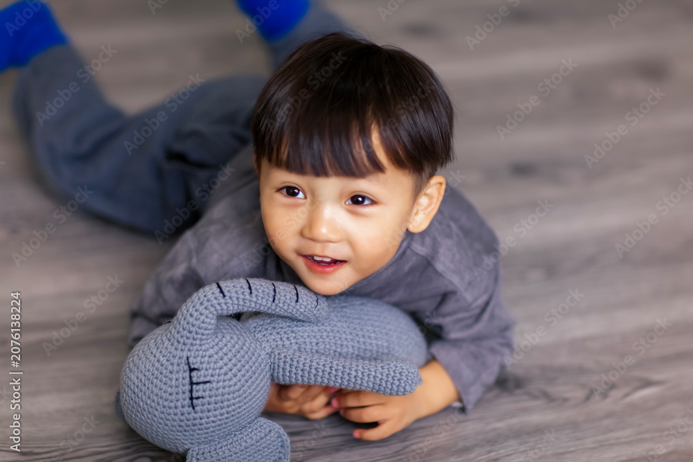Fototapeta premium A cute Asian boy wearing a gray sweater plays indoors.