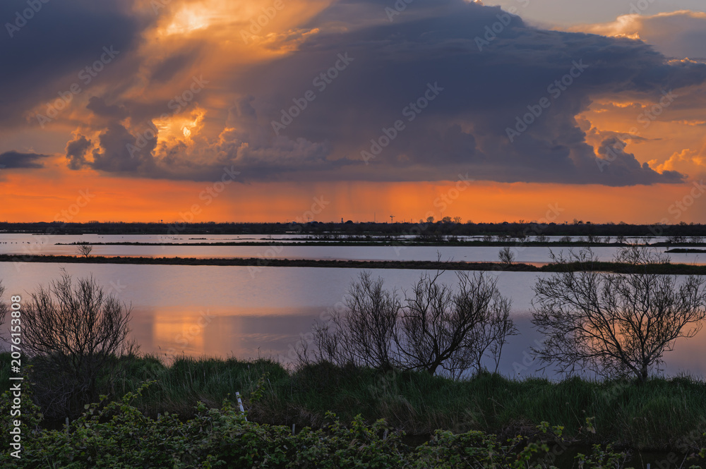 Fototapeta premium sunset over the lagoon inside the river Po delta with a dramatic sky in the background, Porto Levante, Rovigo, Italy