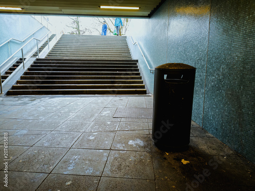 This is an old, polluted underpass with an ugly and dirty garbage can in a big, German city.