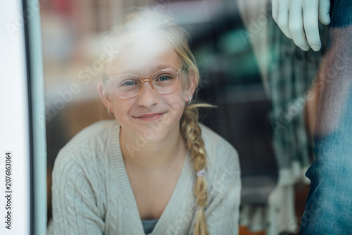 Fotografie Cheerful child wearing eyeglasses gazing through the display window of a fashion boutique while observing the lively street outside