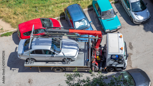 a tow truck lifting or transporting an illegally parked silver sedan from a parking lot