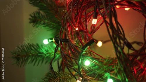 Close up of colorful fairy lights wrapped around a Christmas tree branch.