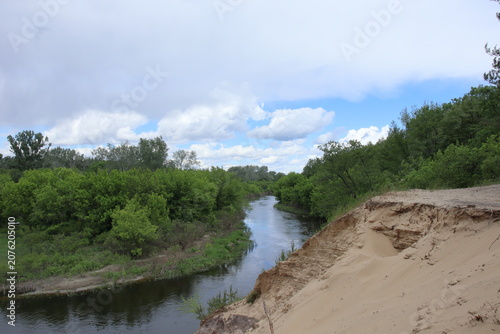 Scenic river winding through green forest with a sandy cliff under a cloudy sky