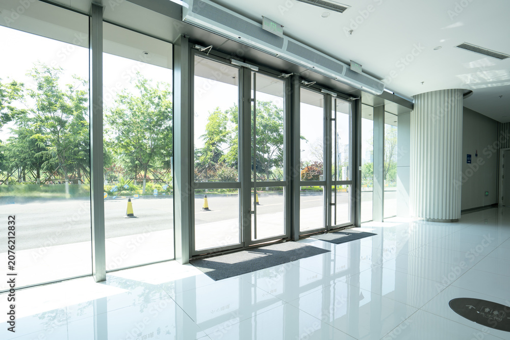 Obraz premium Modern office building entrance hall with glass automatic doors and reflective tiled floor
