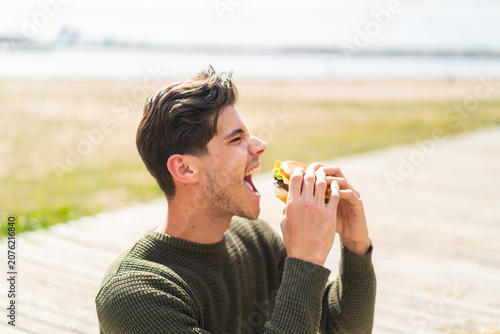 Young caucasian man at outdoors holding a burger