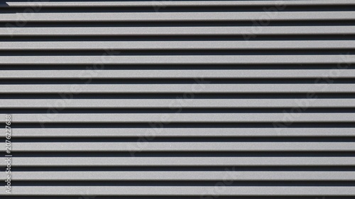 The texture of horizontal metal siding is dark gray. Smooth, parallel panels form a strict geometric pattern, where the alternating protruding edges and deep shadows create volume.