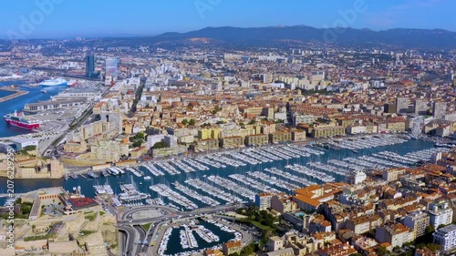 Aerial drone view of the Vieux Port of Marseille with moored yachts, Fort Saint-Jean, the harbor ferris wheel, and CMA CGM Tower in Marseille, France, daytime.