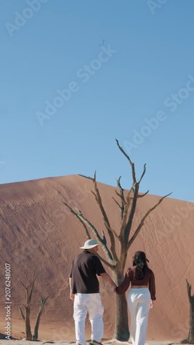 vertical Romantic couple holding hands and walking in Sossusvlei desert, Namibia