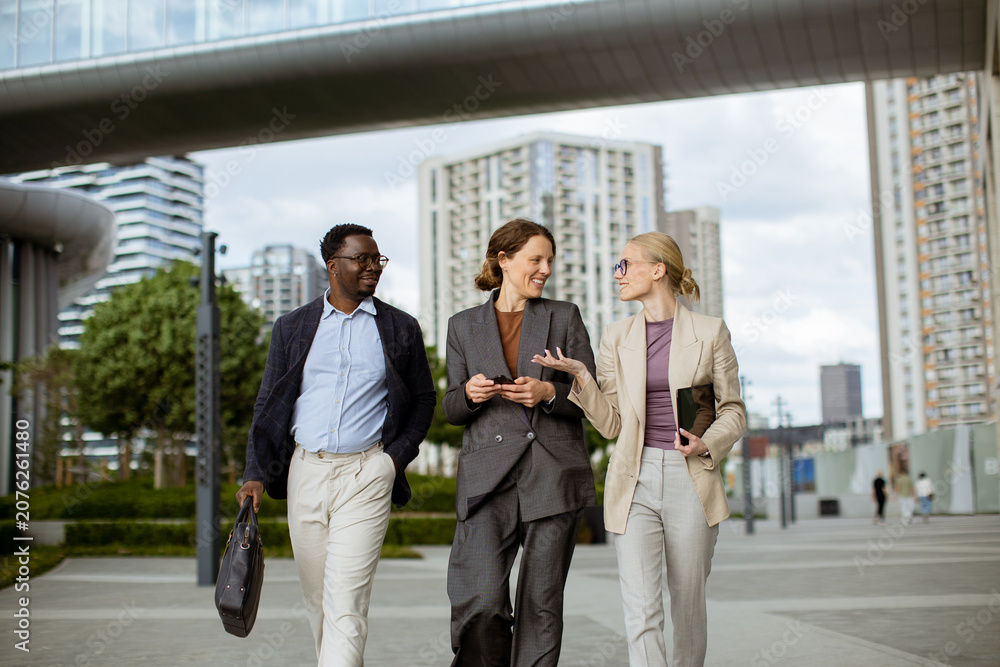 Fototapeta premium Group of three people walk together in a city area during the afternoon