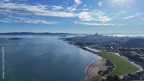 An aerial perspective of the San Francisco bay area, featuring the city skyline, the coastline, and Alcatraz Island under a bright blue sky.