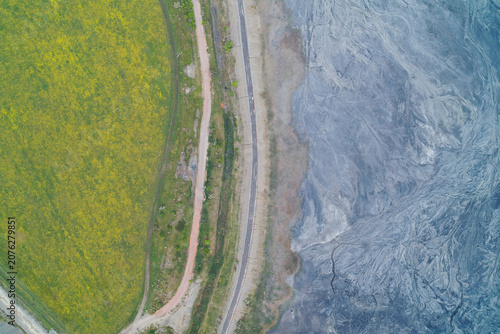 Bild auf Leinwand Industrial slag heap slope with toxic waste erosion runoff next to green agricul