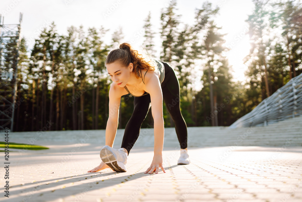 Obraz premium A young athlete trains on steps in the sun's rays. A woman in sportswear stretches or warms up at sunset. The concept of sport, enjoyment, and health.