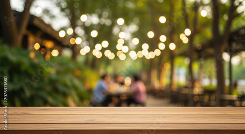Empty wooden table with blurred outdoor cafe and string lights background
