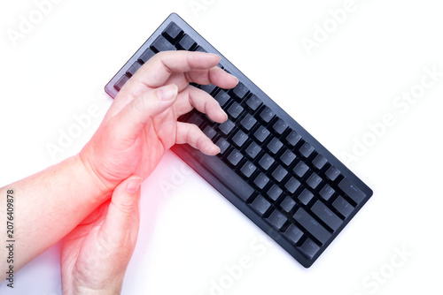 Close-up of a person holding their painful wrist with red highlight accentuating the injury, while typing on a black computer keyboard, isolated on white. Concept of carpal tunnel syndrome