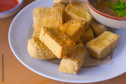Crispy golden deep-fried tofu cubes served on a white ceramic plate with a sweet peanut dipping sauce, a popular traditional Asian appetizer