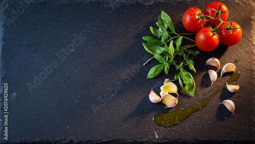 Fresh tomatoes basil garlic and olive oil on dark slate stone background with copy space
