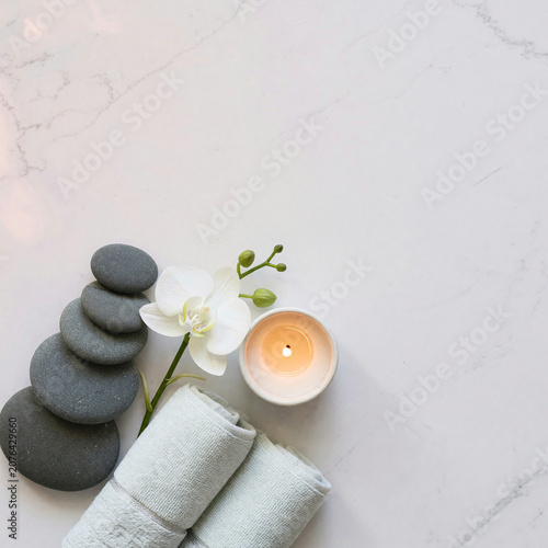 Spa wellness still life with zen stones orchid candle and towels on white marble with copy space