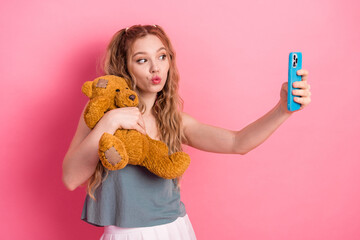 Young woman takes a playful selfie with a teddy bear on a pink background showcasing casual fashion lifestyle and a fun moment