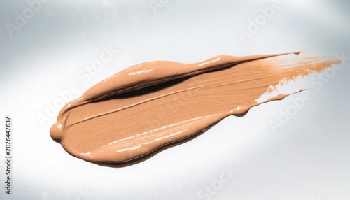 A warm beige liquid foundation smear stretches across a reflective surface, useful for beauty advertising, cosmetic shade guides, and skincare branding.