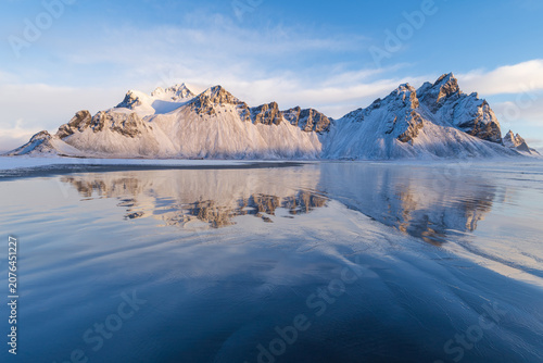 Vestrahorn mountain reflected on wet black sand beach in winter, Iceland