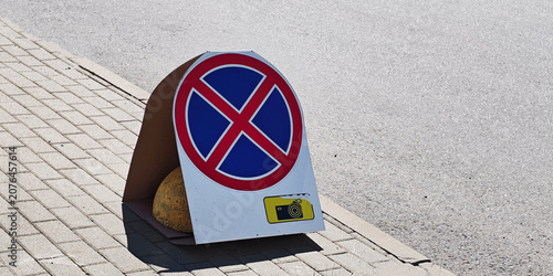 Temporary no stopping sign placed on paved sidewalk, indicating road traffic regulation and camera surveillance zone