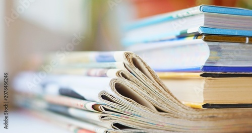 Fotografija Close up stack of daily folded newspapers and colorful books representing tradit