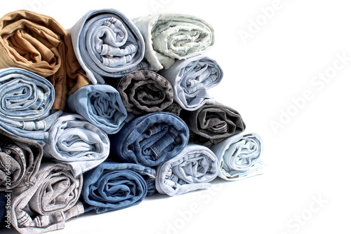Many pairs of denim pants, crumpled into a roll and folded on top of each other, lie on a white background.