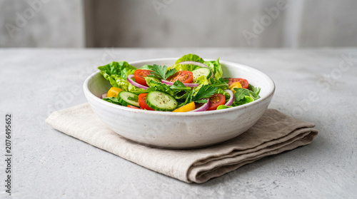 Obraz na płótnie White ceramic bowl filled with a fresh garden salad of crisp lettuce, cucumbers, colorful tomatoes, and red onions rests on a folded linen napkin