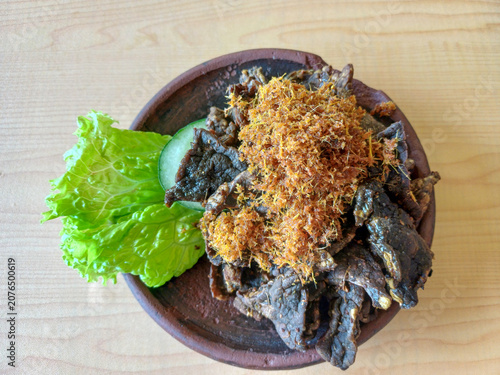 Fried beef lung or paru goreng served with spiced coconut flakes, cucumber slice, and lettuce on clay plate. Indonesian traditional culinary food top view.