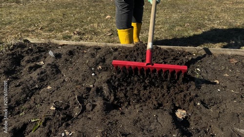 Garden rake in hands of human loosening ground, standing on grass. Soil treatment using agricultural object in spring.