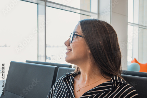 Bilde på lerret Young woman wearing glasses and a striped shirt, sitting in an airport terminal,