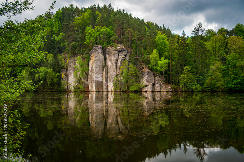 Iconic sandstone cliffs reflected in the calm waters of Vezicky Pond (Vezicky rybnik in czech) in the beautiful Bohemian Paradise, Czech Republic, a famous scenic destination popular with tourists.