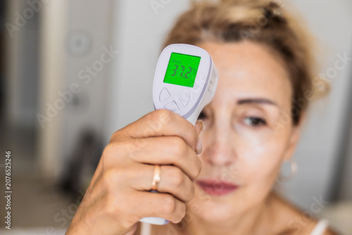 Obraz na plátně Mature Caucasian woman checks her temperature with a digital thermometer