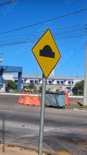 Traffic warning sign for speed bump standing on a sidewalk near the street