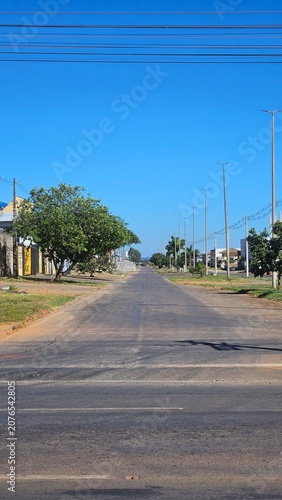 Empty asphalt road in a quiet suburban neighborhood under a clear blue sky