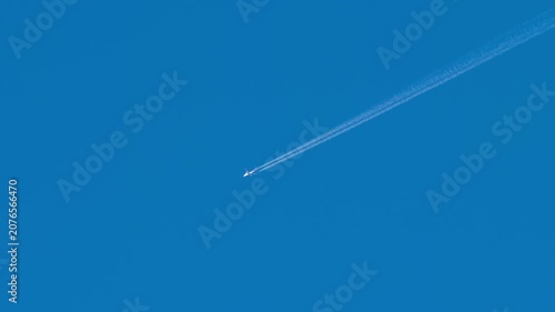 Commercial airplane flying at high altitude leaving a long white contrail in a clear blue sky, bright sunny day, telephoto lens shot