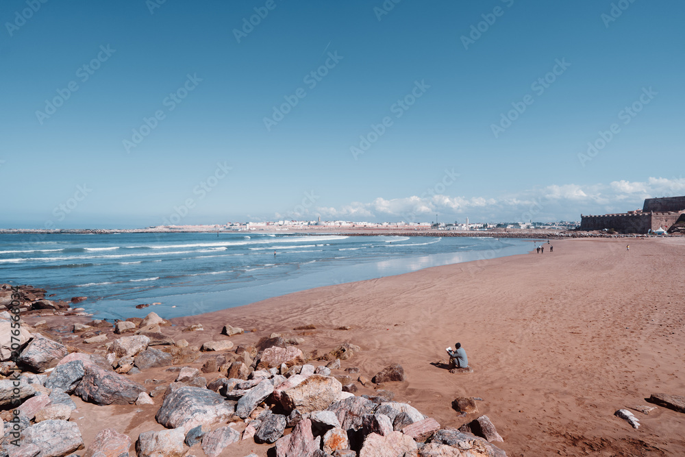 Obraz premium Vast sandy shoreline extending alongside a calm blue ocean, under a clear expansive sky. Scenic Coastal View with Sandy Beach and Blue Sky Horizon