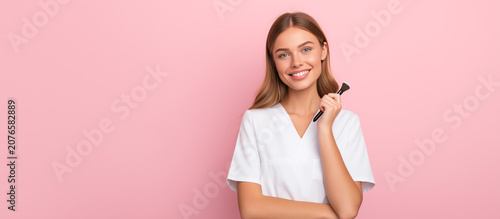 Smiling Female Cosmetologist in White Medical Coat on Pink Background with Copy Space
