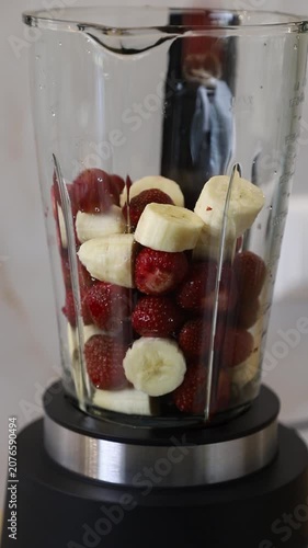 Making a healthy fruit smoothie (milkshake) with fresh strawberries and bananas in a kitchen blender
