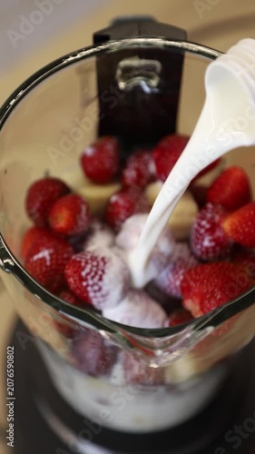 Fresh milk pouring into a blender with strawberries and bananas to prepare a healthy smoothie (milkshake)
