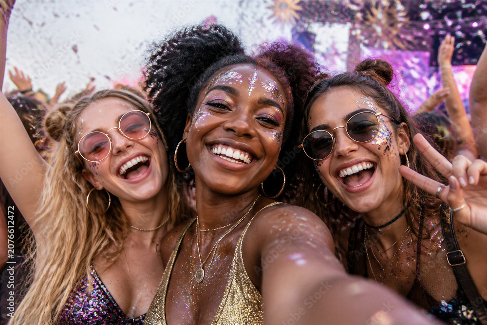 Fototapeta premium Group of young women smiling and taking selfie at festival outdoor celebration