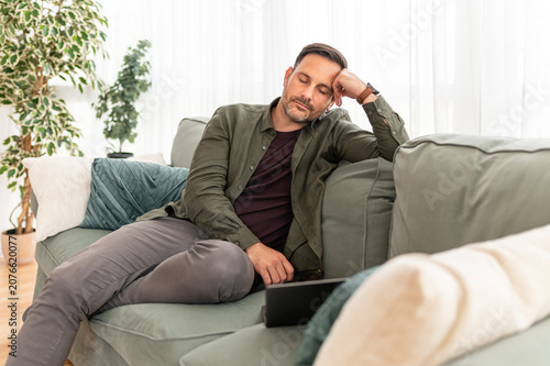 Man resting on a couch at home, experiencing fatigue and mental exhaustion, taking a brief pause from work, needing a moment of relaxation and self care