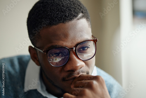 Close up of young Black man wearing eyeglasses, thinking while viewing screen, conveying focus and decision making. Useful for business strategy, office work, productivity