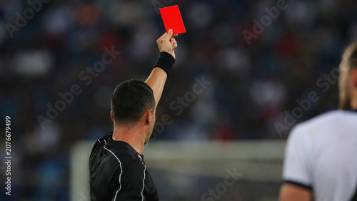 Referee showing a red card during a soccer match with blurred stadium background
