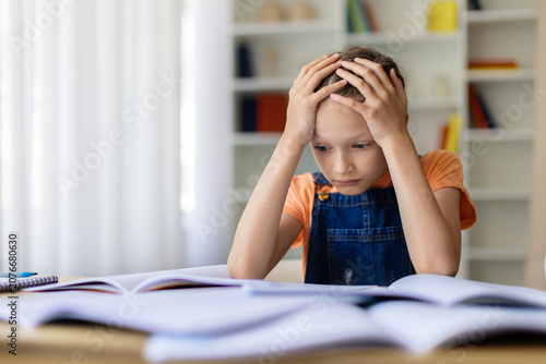 Photos Teen girl holding her head while studying with open books at home, showing homew