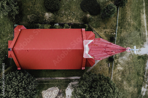 Aerial view of Rucava evangelical lutheran church with its red roof set amidst green trees and surrounding landscape in Rucavas pagasts, Dienvidkurzemes novad, Latvia.