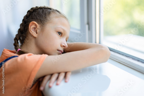 Foto Pensive teen girl leaning on windowsill at home and looking outside, showing lon