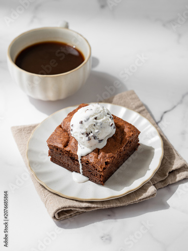 A piece of chocolate brownie with ice cream on a plate and a cup of espresso coffee